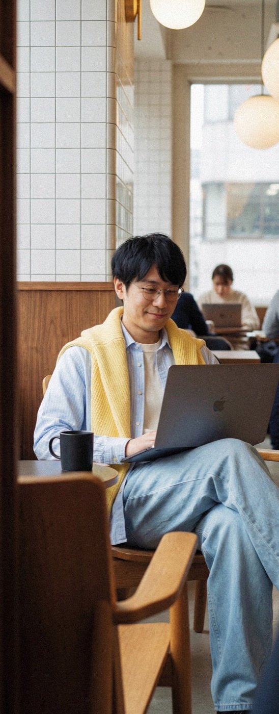 Person in yellow scarf working on a laptop in a warm cafe with hanging globe lights
