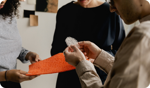Three professionals collaborating and examining unique material samples in a creative workspace