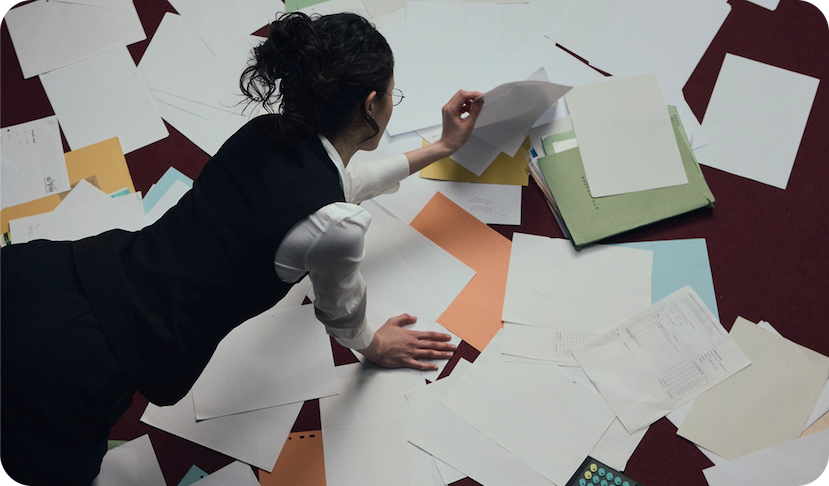 Woman in business attire surrounded by scattered papers and documents on a desk, illustrating work overwhelm and energy drain