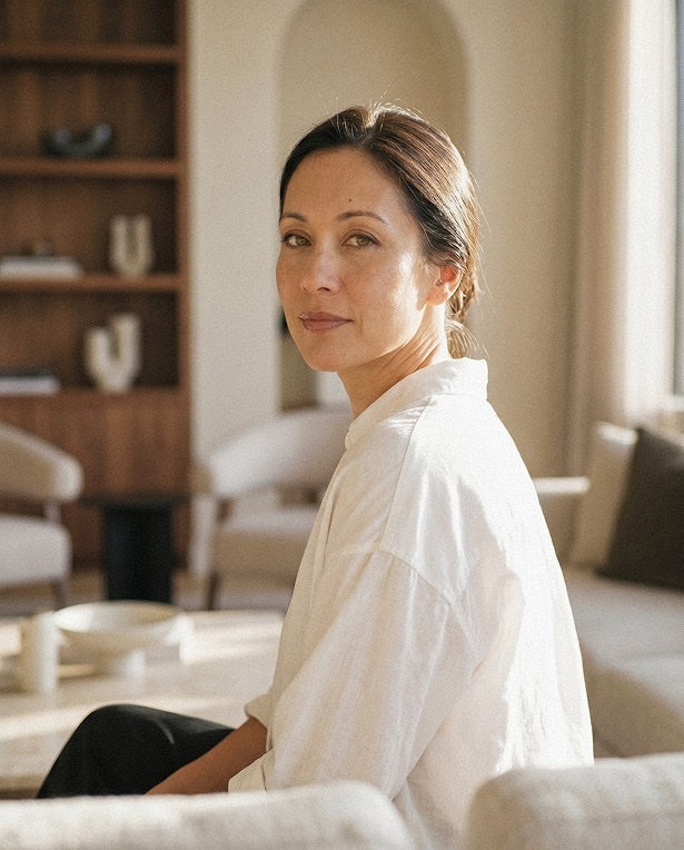 Person seated on a cream sofa with bookshelves behind, looking thoughtfully toward camera.