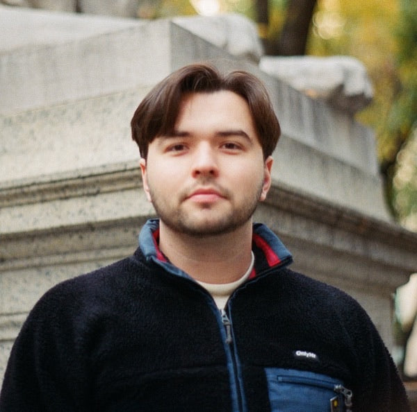 Becker Goldstein, dark hair and short beard in a navy fleece, outdoors by stone architecture