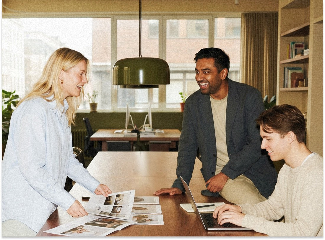 Three colleagues collaborating around a table in a bright office, reviewing reports