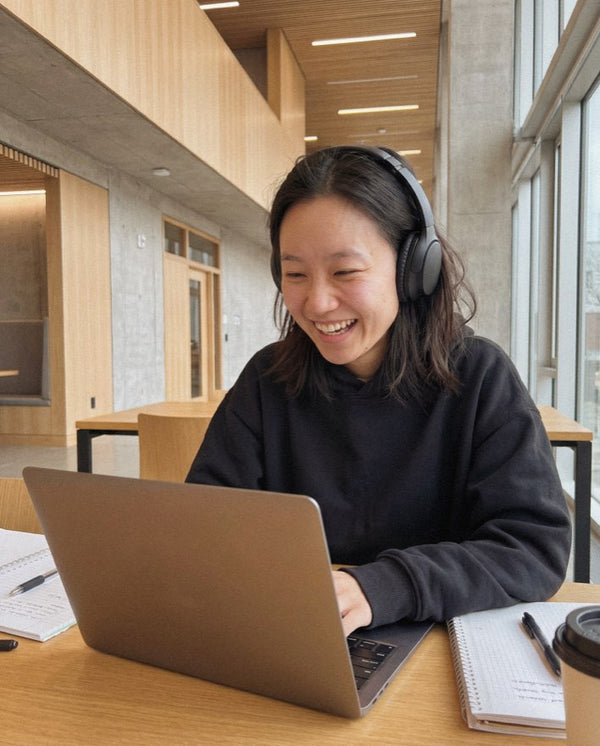 Smiling woman in headphones working on a laptop in a bright study space